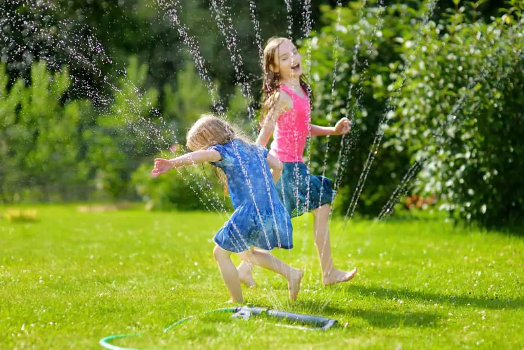 Adorable little girls playing with a sprinkler in a backyard on sunny summer day