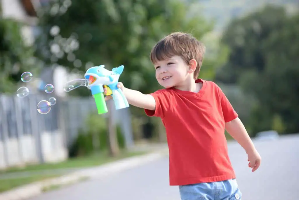 Little boy playing with soap bubbles machine on the street.